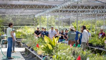 AIR team standing in front of onlooking audience members surrounded by nursery plants growing on benches